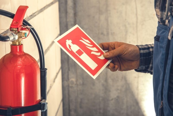 Regulatory reform fire safety order 2005, illustrated by a person holding a fire safety sign beside a wall-mounted fire extinguisher.